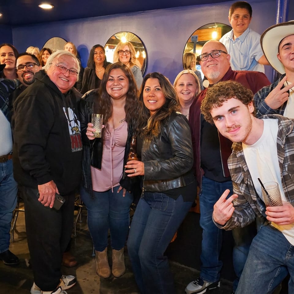 Group of people posing together inside a lively restaurant, with several guests wearing cowboy hats and holding drinks.